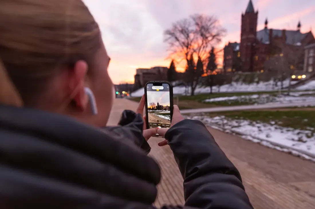 A person taking a picture of the sunset on campus.